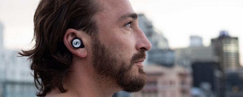 En man bär Sennheiser Momentum True Wireless 3-hörlurar i en stadsmiljö.