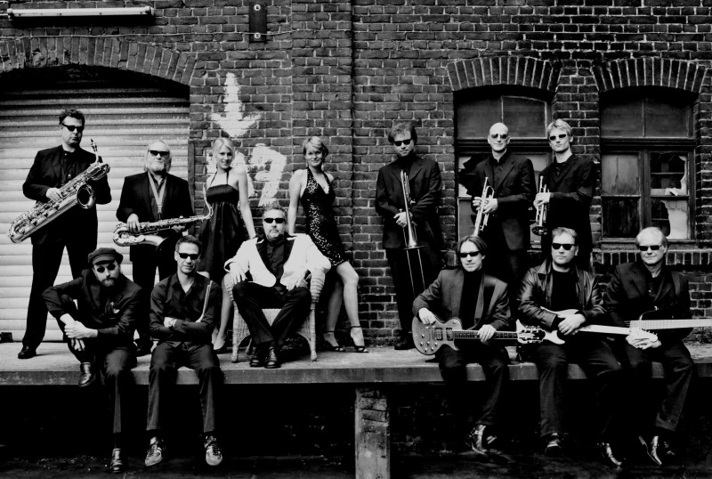 Ett stilrent rhythm and blues-band poserar framför en tegelvägg inför B&W Rhythm 'n' Blues-festivalen.