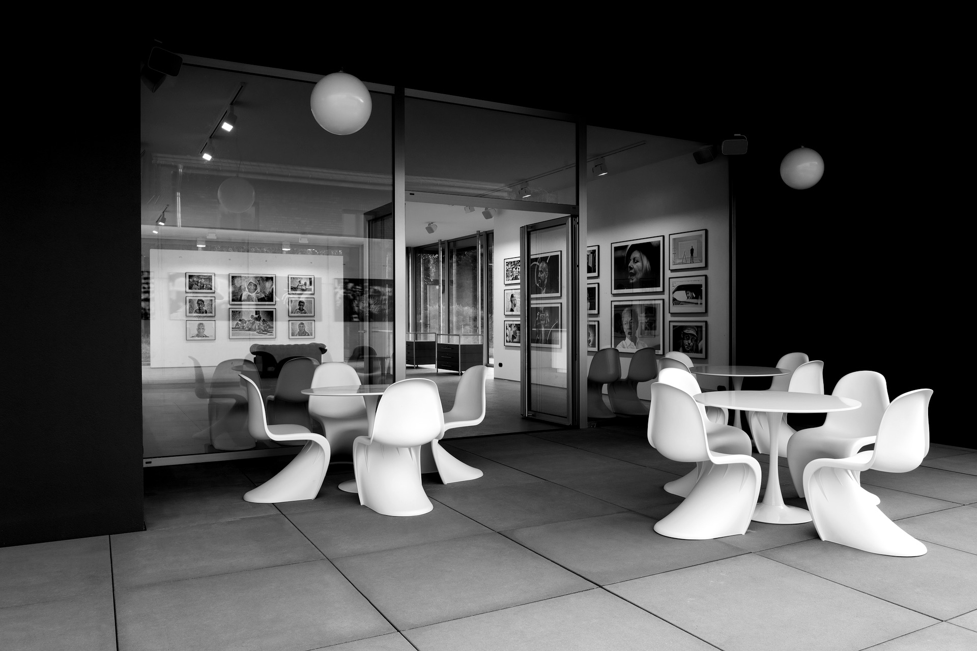 Modern konstgalleri med vita stolar och bord, svartvita fotografier på väggarna skapar en elegant atmosfär.