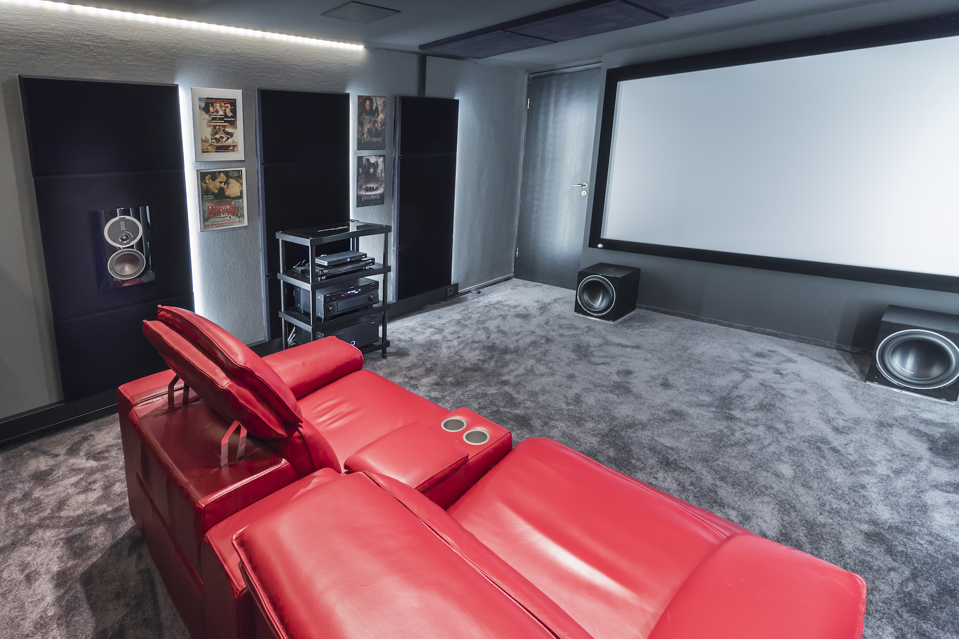 Mysigt hemmabio med röd lädersoffa, stor skärm och surroundljud, perfekt för filmkvällar med vänner och familj.