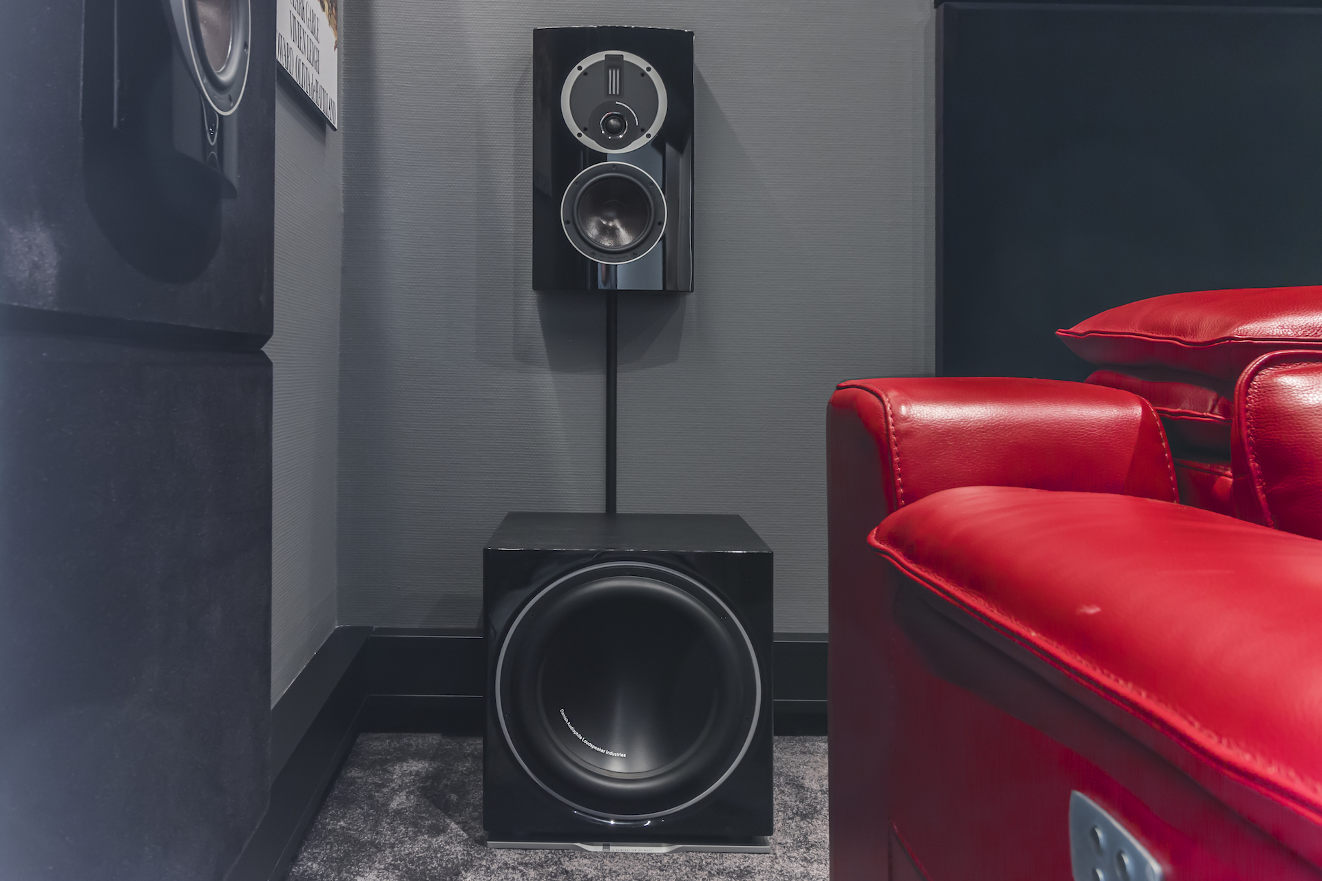 Hemmabiohörna med kraftfullt ljudsystem, elegant högtalare och subwoofer samt en bekväm röd läderfåtölj.
