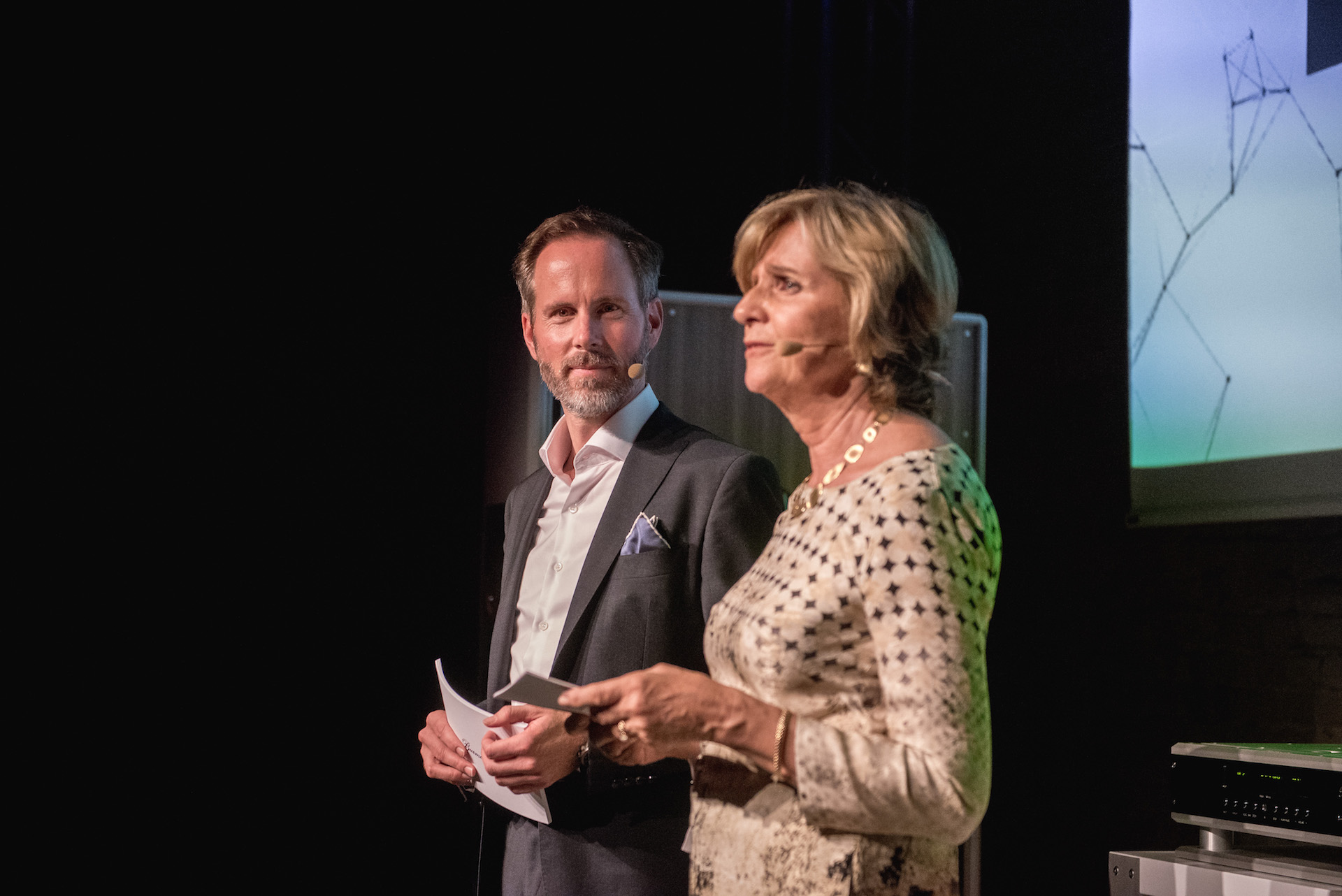 Två moderatorer presenterar på scenen vid ett evenemang hos Burmester.