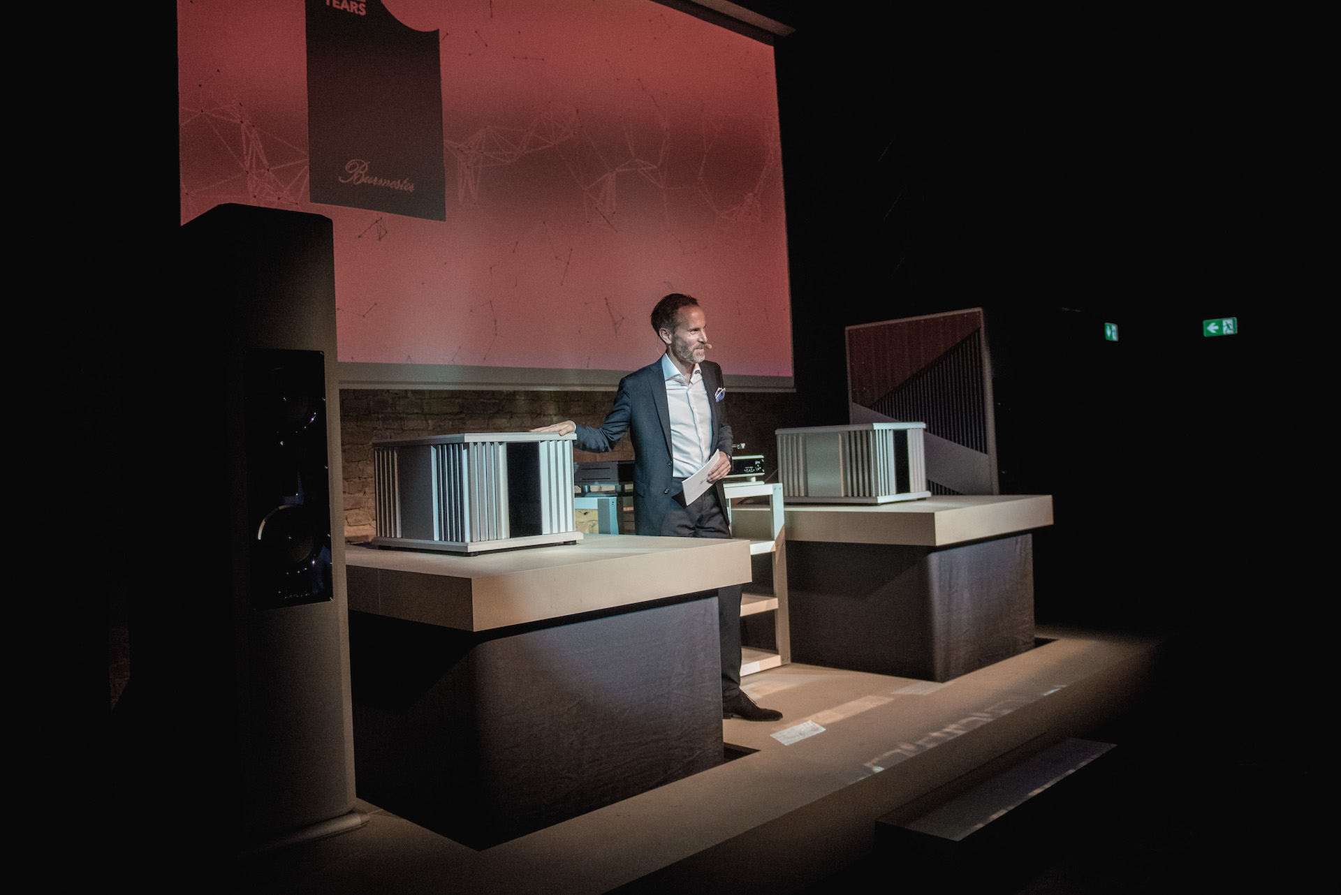 En talare presenterar Burmesters senaste ljudprodukter på scen under ett 40-årsjubileum för innovation inom ljudteknik.