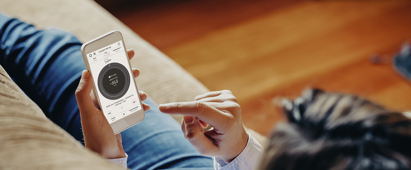 Person styr Lyngdorf TDAI-1120 streamingförstärkare med smartphone, vilket ger enkel användning och modern design.